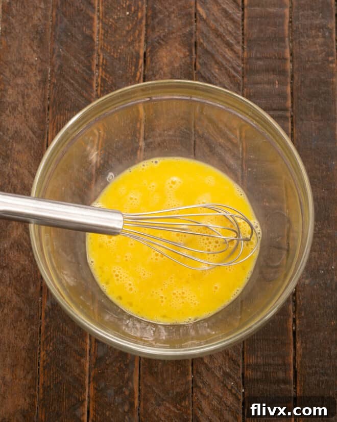 Step 1: Fresh eggs being whisked vigorously in a mixing bowl until light and foamy.