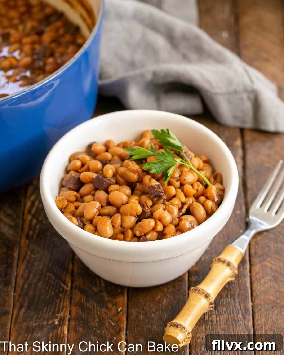 A beautiful white bowl brimming with homemade Boston baked beans, garnished with a bamboo fork on the side, ready to be enjoyed.