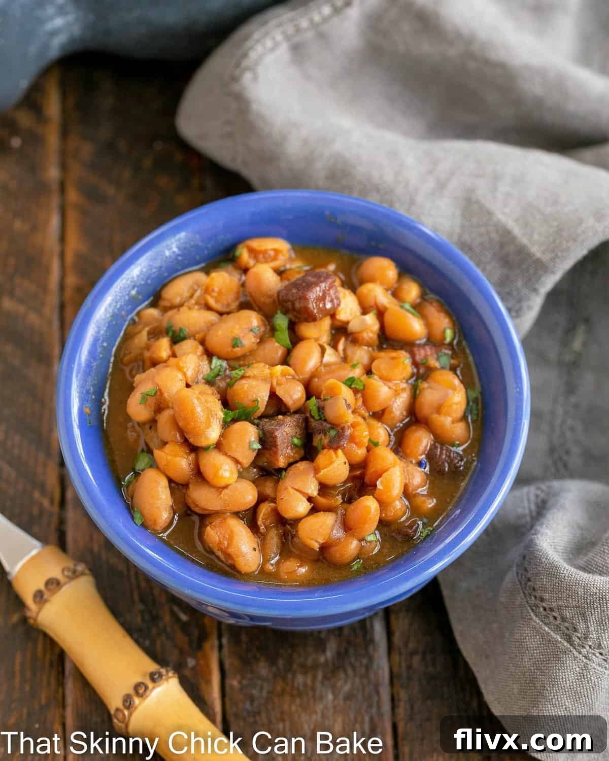 A rustic blue ceramic bowl filled to the brim with comforting homemade baked beans, presented with a bamboo fork.