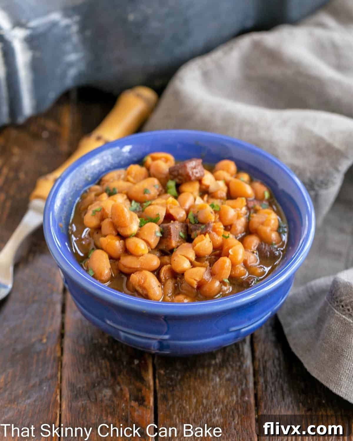 A pristine blue ceramic bowl filled to the brim with richly sauced homemade baked beans, ready to be served.