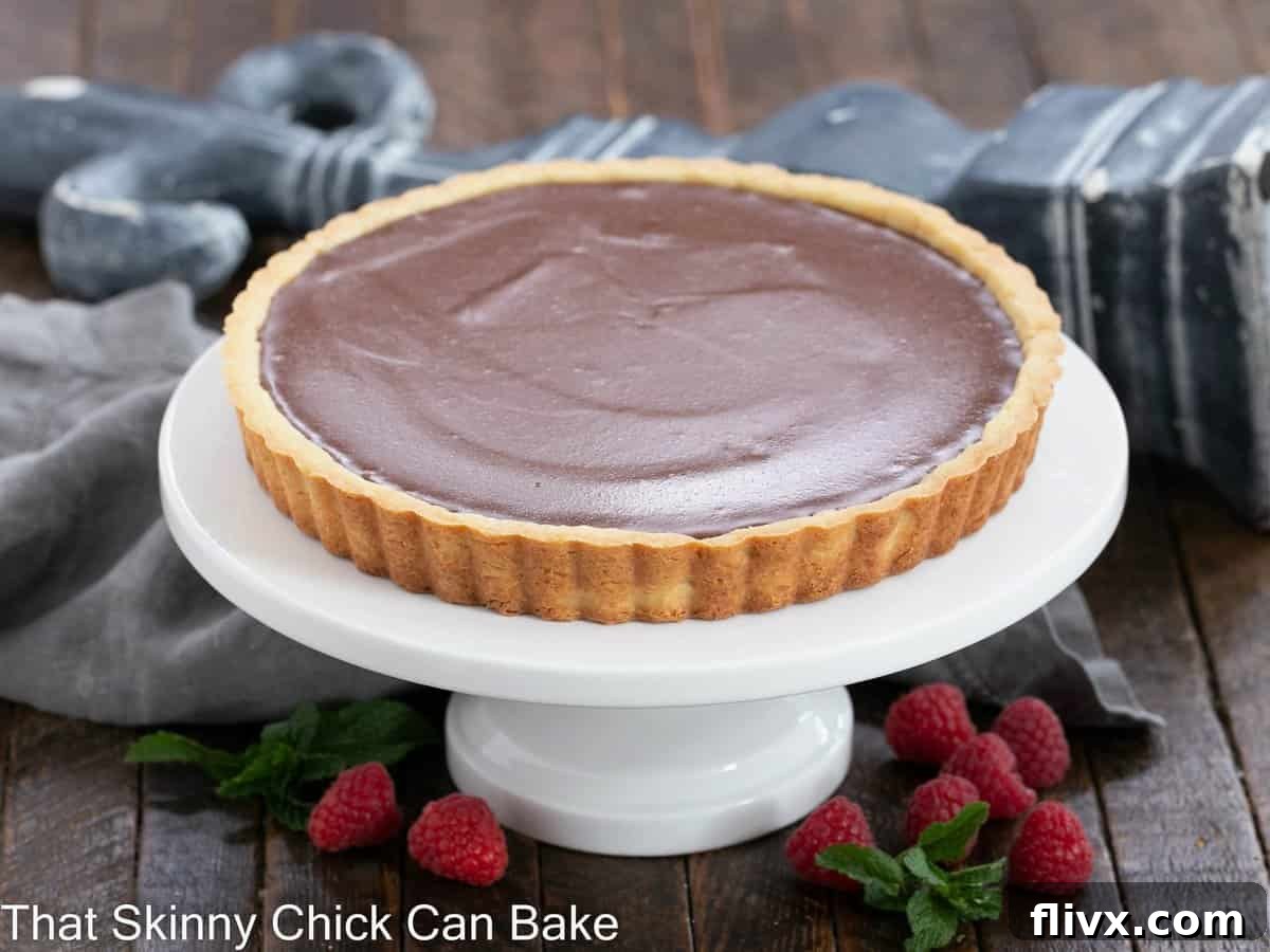 A whole, beautifully presented milk chocolate tart on a pristine white cake stand, ready to be served.
