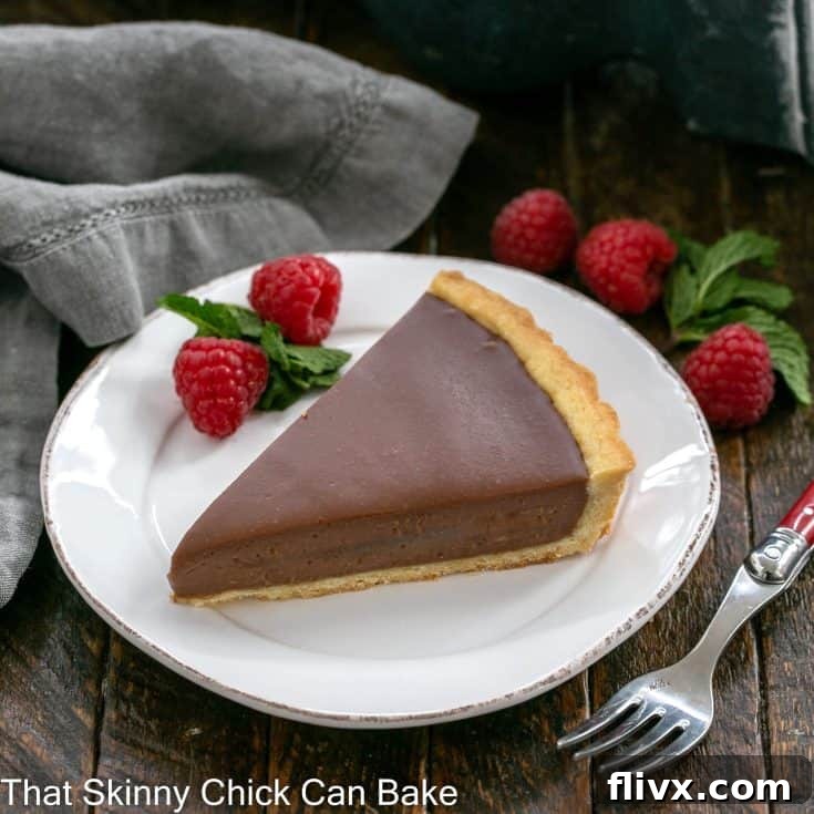 A wedge of milk chocolate tart on a white dessert plate with raspberry garnish and a red handle fork
