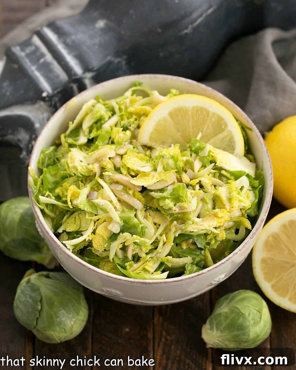 Shaved Brussels sprouts salad in a white serving bowl, garnished with almonds and parmesan cheese.