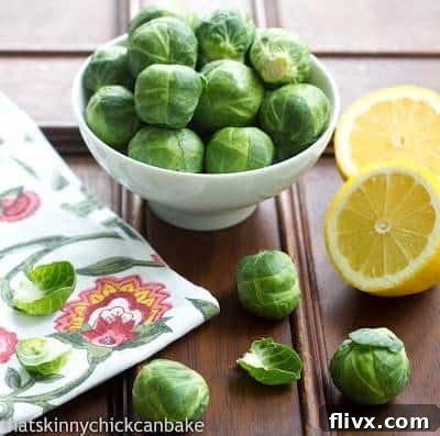 Brussels Sprouts in a small white bowl next to sliced lemons on a wooden table.