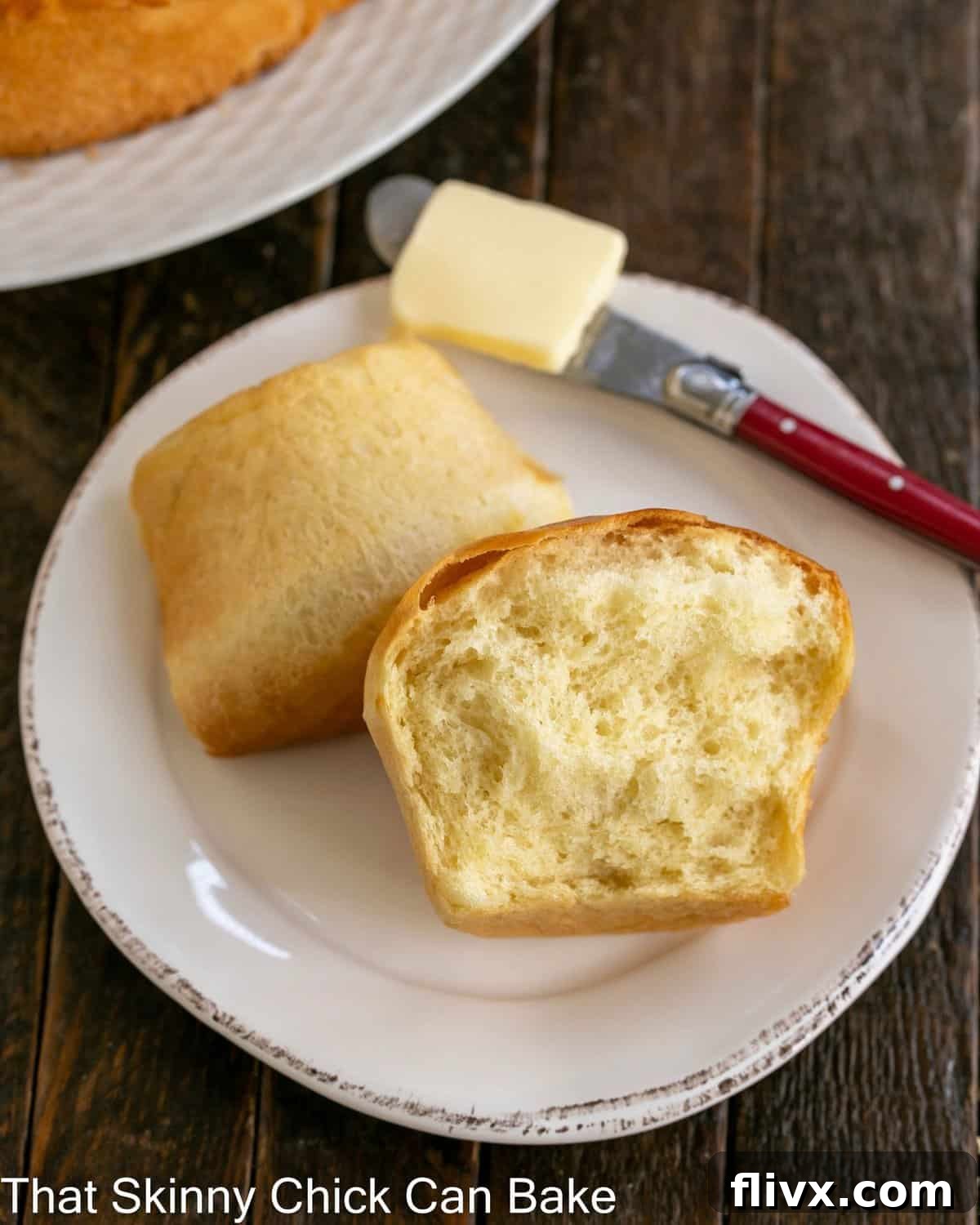 A Japanese Milk Bread Bun torn in half on a small white plate with a red butter knife.