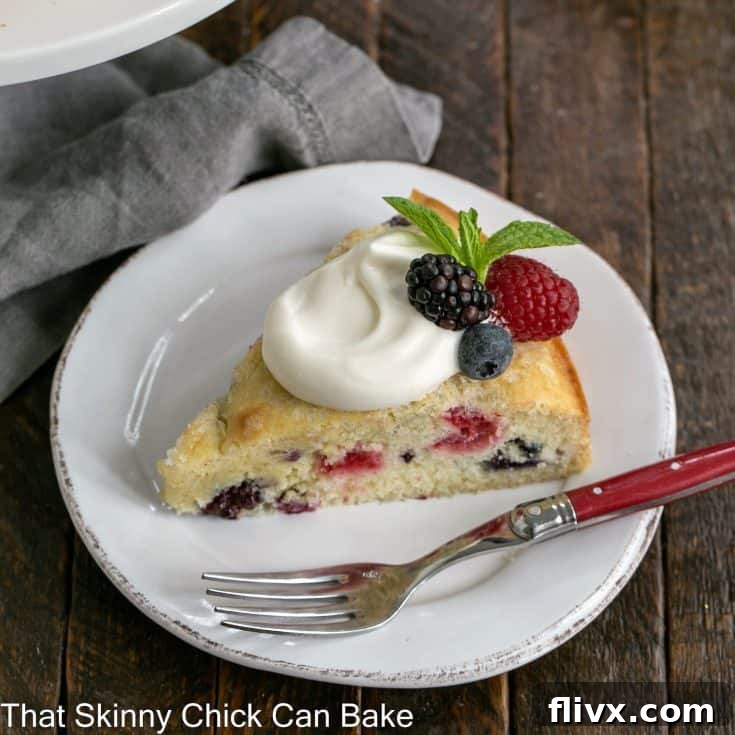 A vibrant slice of mixed berry cake crowned with a swirl of light lemon cream and garnished with fresh berries, all resting on a white plate. This image captures the essence of a refreshing and elegant dessert.