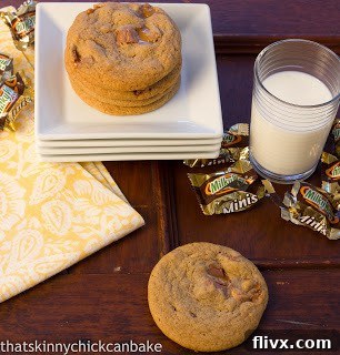 Milky Way Cookies on a stack of white serving plates next to Milky Way wrappers and a glass of milk. 