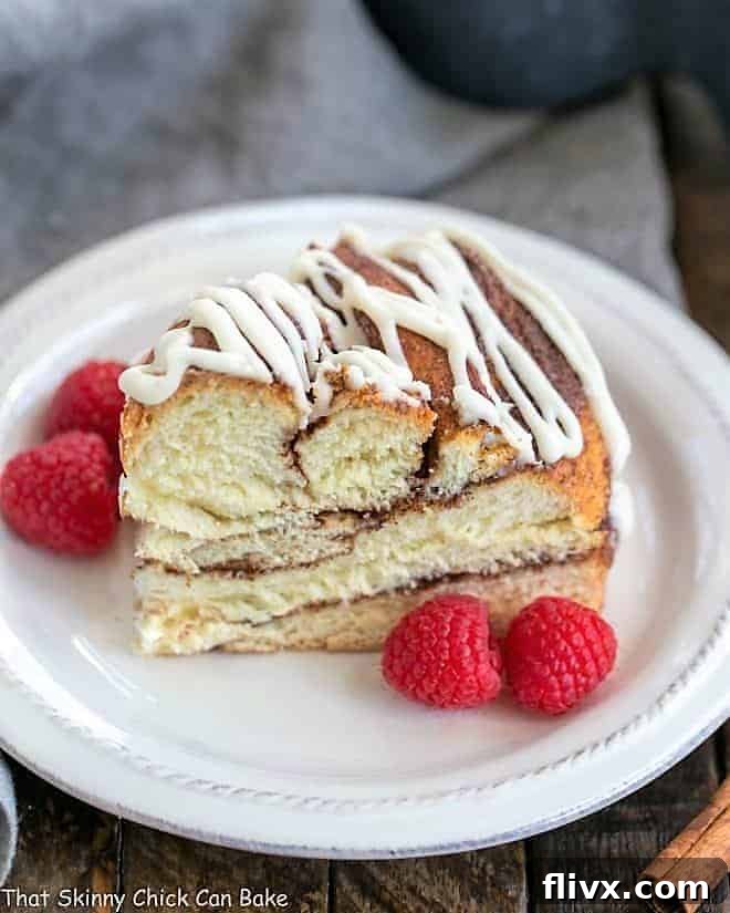 A perfectly sliced Cinnamon Twist Bread on a white plate, adorned with fresh red raspberries. The golden crust, visible layers of cinnamon swirl, and soft interior promise a delightful experience.