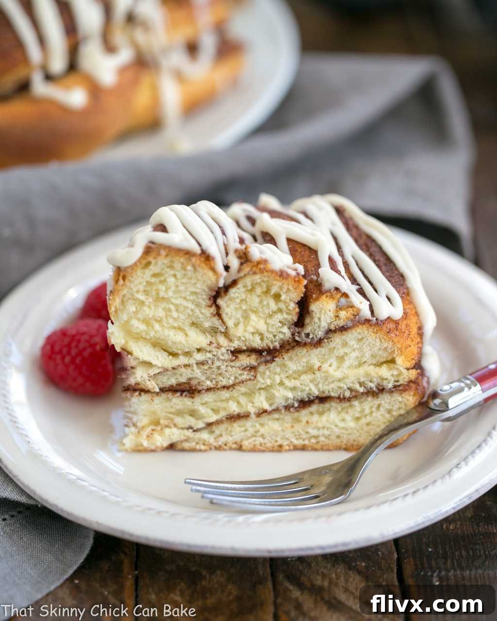 A close-up shot of a thick slice of Cinnamon Twist Bread on a white plate, revealing its soft, airy texture and generous cinnamon swirls. A red-handled fork rests beside it, ready for indulgence.