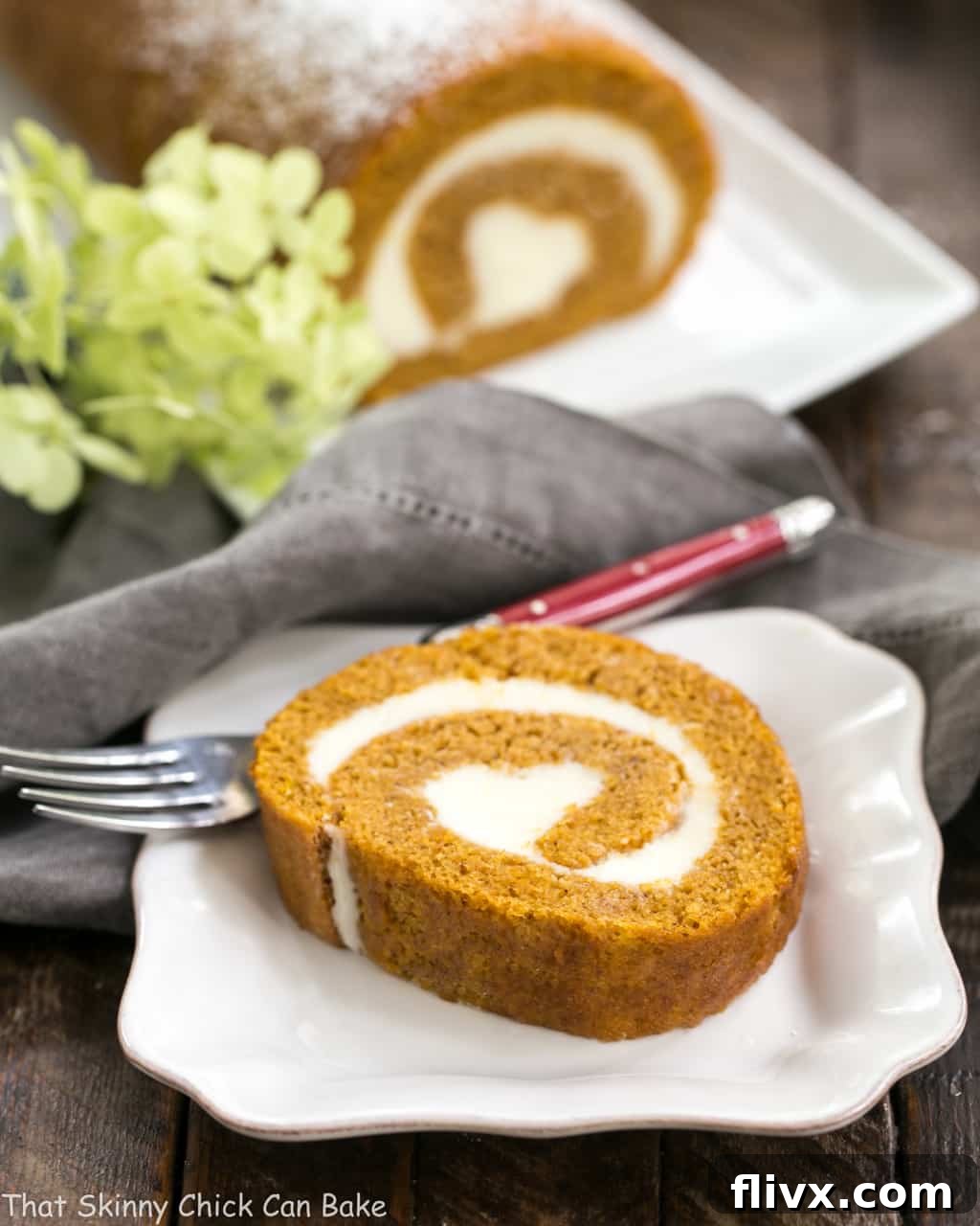 A close-up of a perfectly sliced Old Fashioned Pumpkin Roll, revealing a beautiful swirl of vibrant pumpkin cake and creamy white cream cheese filling on a simple white ceramic plate.