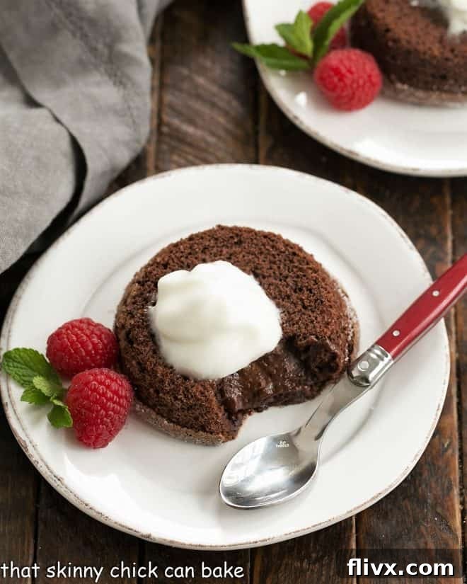 Overhead view of a chocolate lava cake topped with Kahlua whipped cream on a white plate with a raspberry and mint garnish and a red handle spoon, highlighting the molten center.