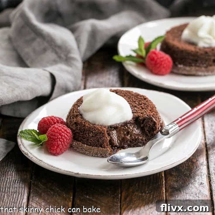 Two perfectly baked chocolate lava cakes on white dessert plates, elegantly garnished with fresh mixed berries, vibrant mint leaves, and a generous dollop of fluffy Kahlua-infused whipped cream. The image highlights the rich dark chocolate of the cakes against the bright, fresh toppings, inviting viewers to indulge.