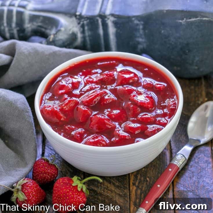 A beautifully presented bowl of fresh strawberry compote with a red-handled spoon beside it, set against a light background.