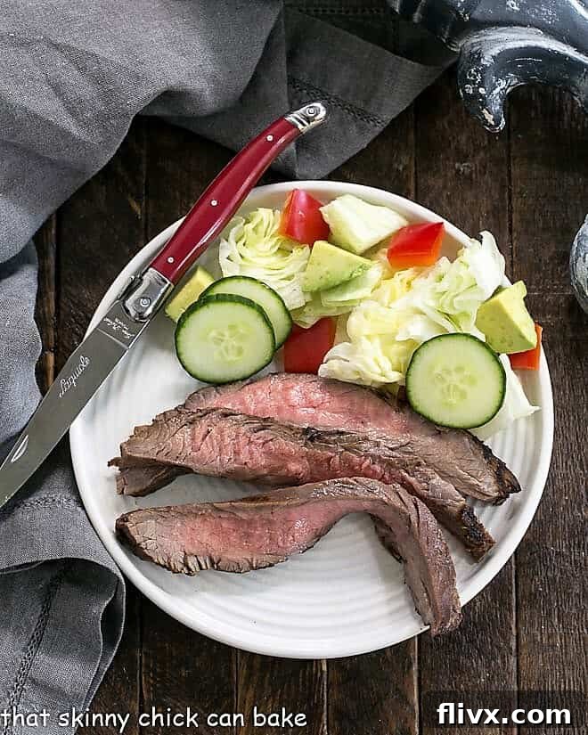 Flank steak marinated in a Soy, Orange Juice, Red Wine Marinade sliced on a round white plate, showing the tender texture.