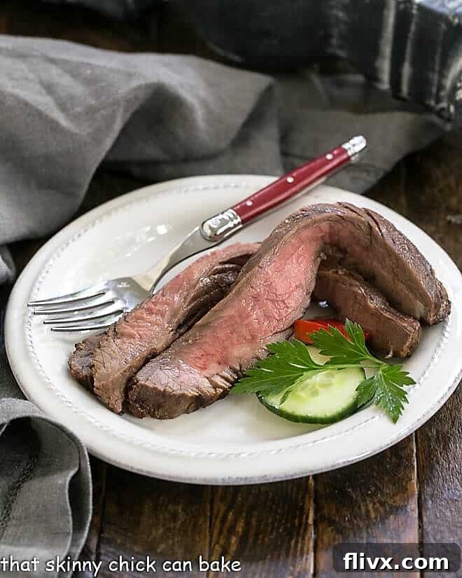 Perfectly grilled slices of flank steak on a white plate with a red handled fork, ready to eat.