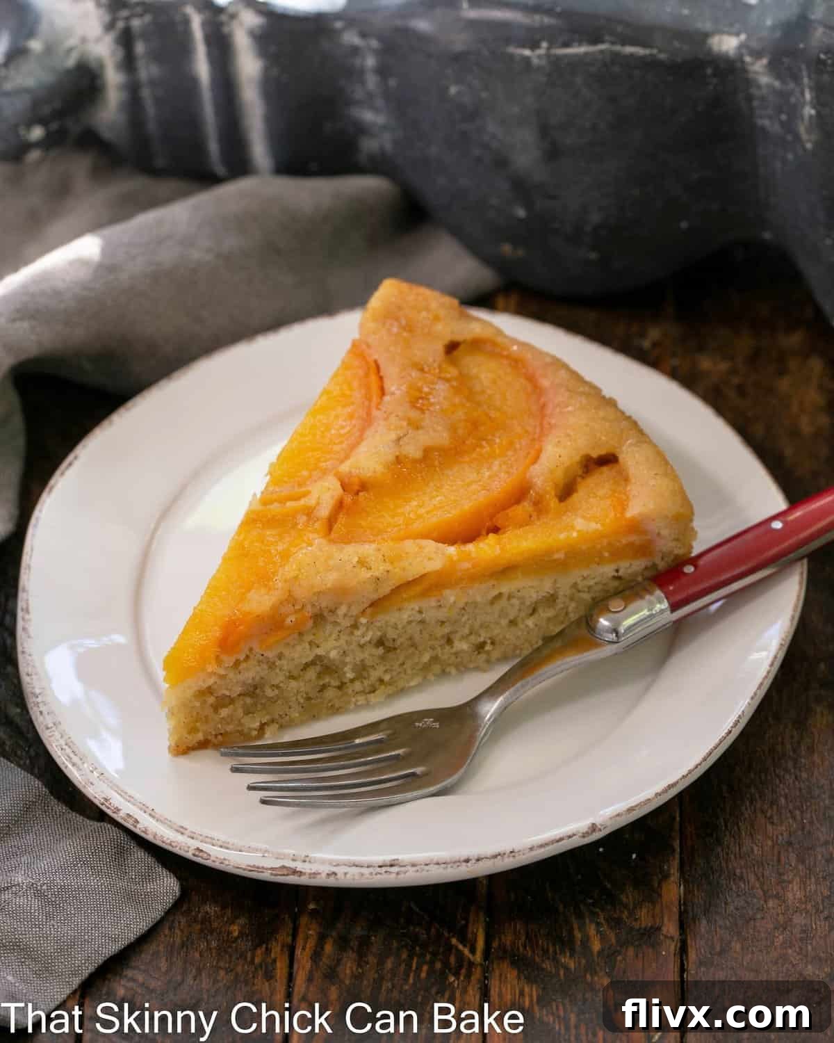 A slice of peach upside down cake on a white dessert plate with a red handle fork.