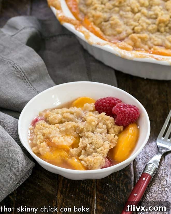 A serving of peach raspberry crisp in a dessert bowl, garnished with a red handled fork, inviting a sweet indulgence.