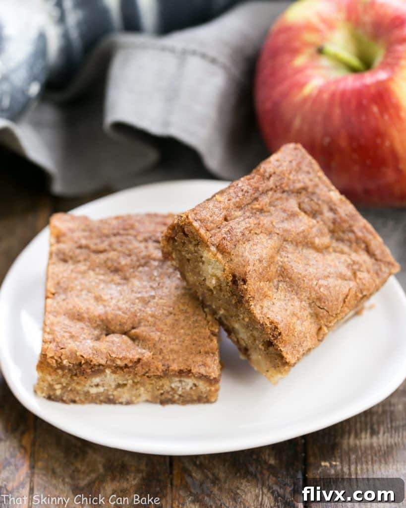Delicious Cinnamon Apple Blondies (also known as Apple Brownies) on a white tear-shaped ceramic plate, garnished with a sprinkle of cinnamon and a few apple slices.
