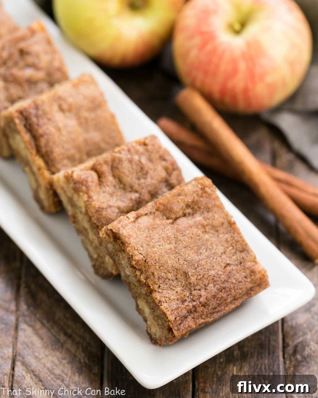 Squares of freshly baked Cinnamon Apple Blondies arranged neatly on a white ceramic platter, highlighting their moist, dense texture and visible apple chunks.