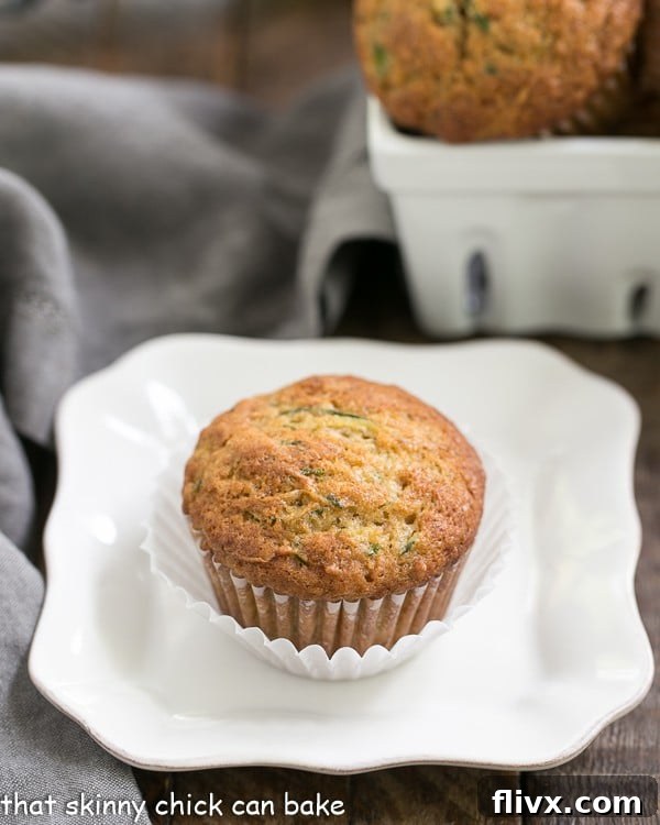 Three Cinnamon Zucchini Muffins arranged on a white plate, with a basket of more muffins in the blurred background, showcasing their golden-brown tops.