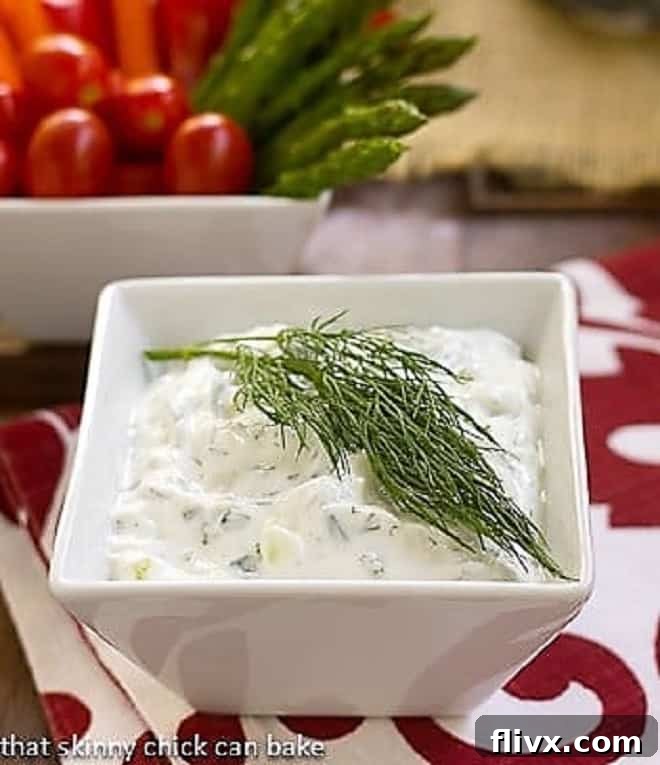 Authentic Greek Tzatziki - a versatile, creamy Greek yogurt sauce brimming with fresh herbs, crisp cucumber, and aromatic garlic, perfect for dipping or as a condiment. Creamy Greek Tzatziki Sauce in a pristine white square bowl, garnished with fresh dill sprigs and a drizzle of olive oil, ready to be served.