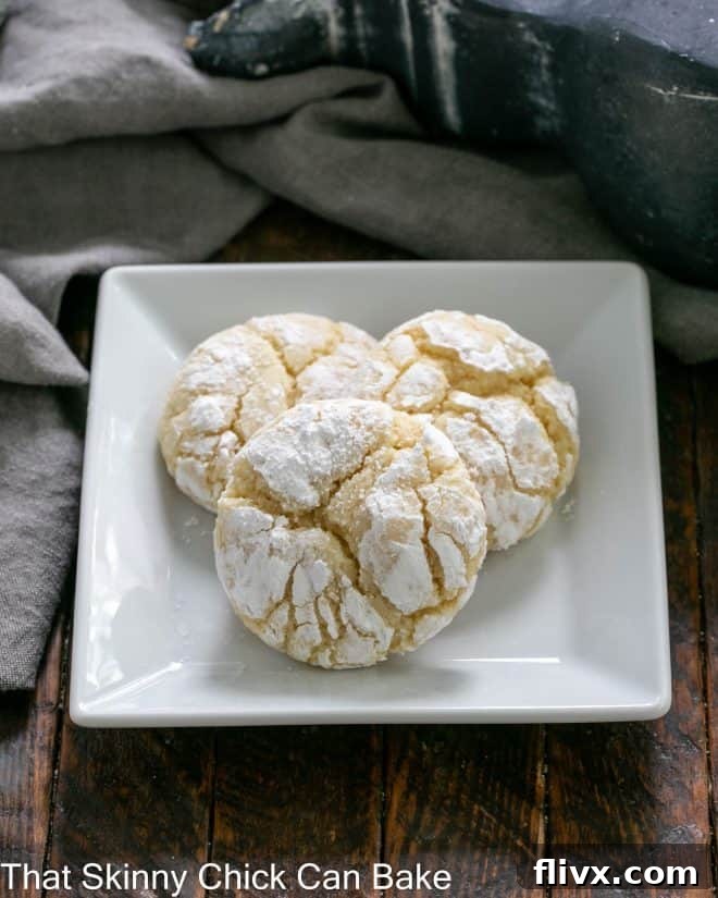 Three golden brown gooey butter cookies arranged elegantly on a square white plate, showing their distinctive crackled tops.
