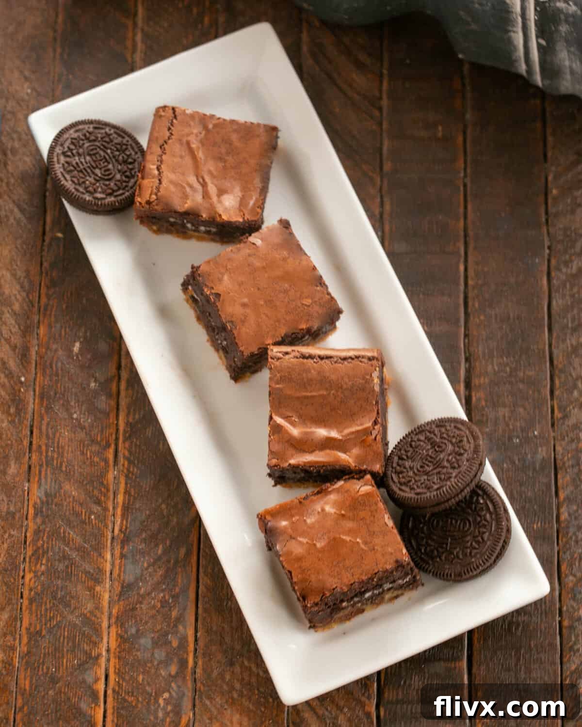 Four perfectly cut chocolate chip Oreo cookie brownies displayed on a white ceramic tray, garnished with whole Oreos.