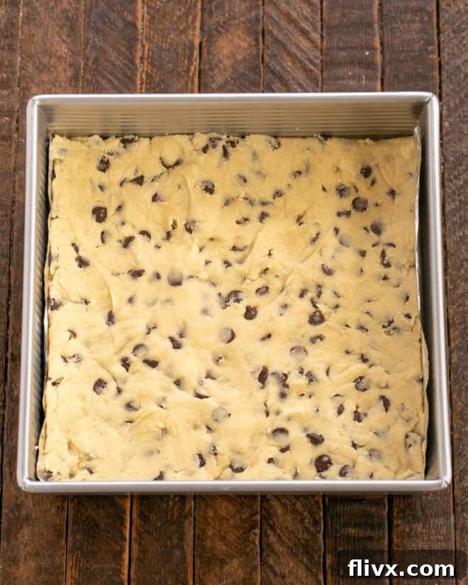 Cookie dough spread evenly in the bottom of a prepared baking pan.