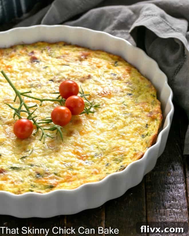 Quiche in a shallow white souffle dish with cherry tomato garnish.