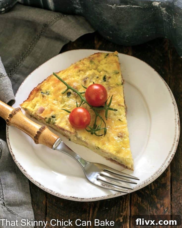 Overhead view of a slice of zucchini quiche on a small white plate with a bamboo handled fork