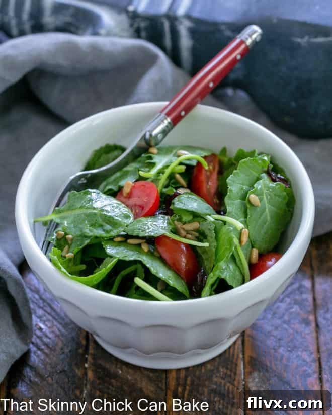 Small white bowl filled with kale salad with a red handled fork.