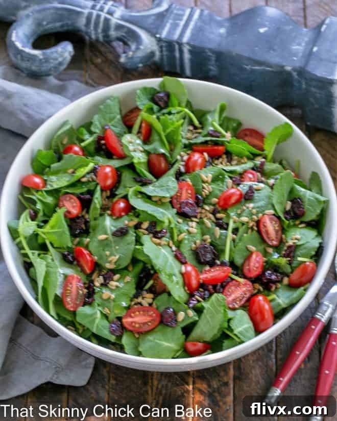 Overhead view of kale salad in a white bowl with red handled serving utensils.