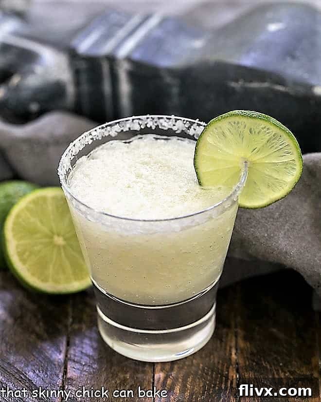 A beer margarita in a high ball glass with a salted rim and thin lime slice garnish.