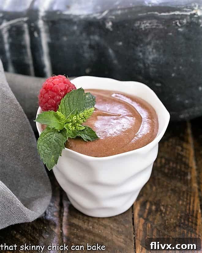 Exquisitely prepared French chocolate mousse in a pristine white bowl, garnished with a vibrant raspberry and a fresh mint sprig.