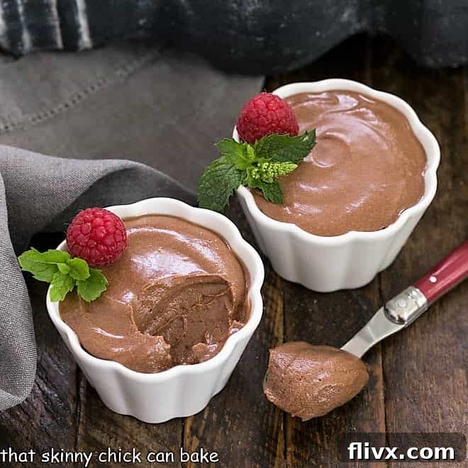 Two elegant white dishes filled with perfectly chilled chocolate mousse, garnished with a vibrant raspberry and a fresh mint leaf, ready for serving.