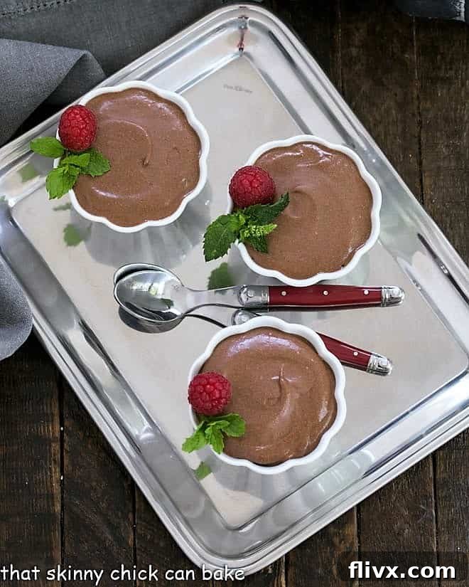 Three perfectly portioned cups of French chocolate mousse, garnished, presented on a elegant silver tray with two tasting spoons, ready for enjoyment.