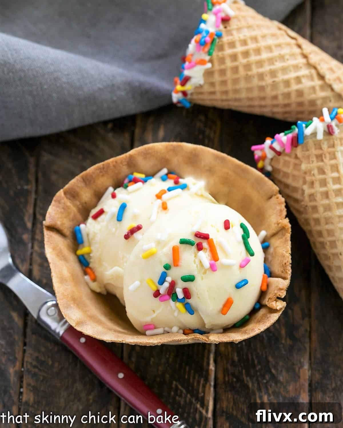 Two delightful sugar cones, one adorned with a vibrant array of sprinkles, sit alongside a glass dish filled with creamy cake batter ice cream and more sprinkles, inviting a celebratory treat.