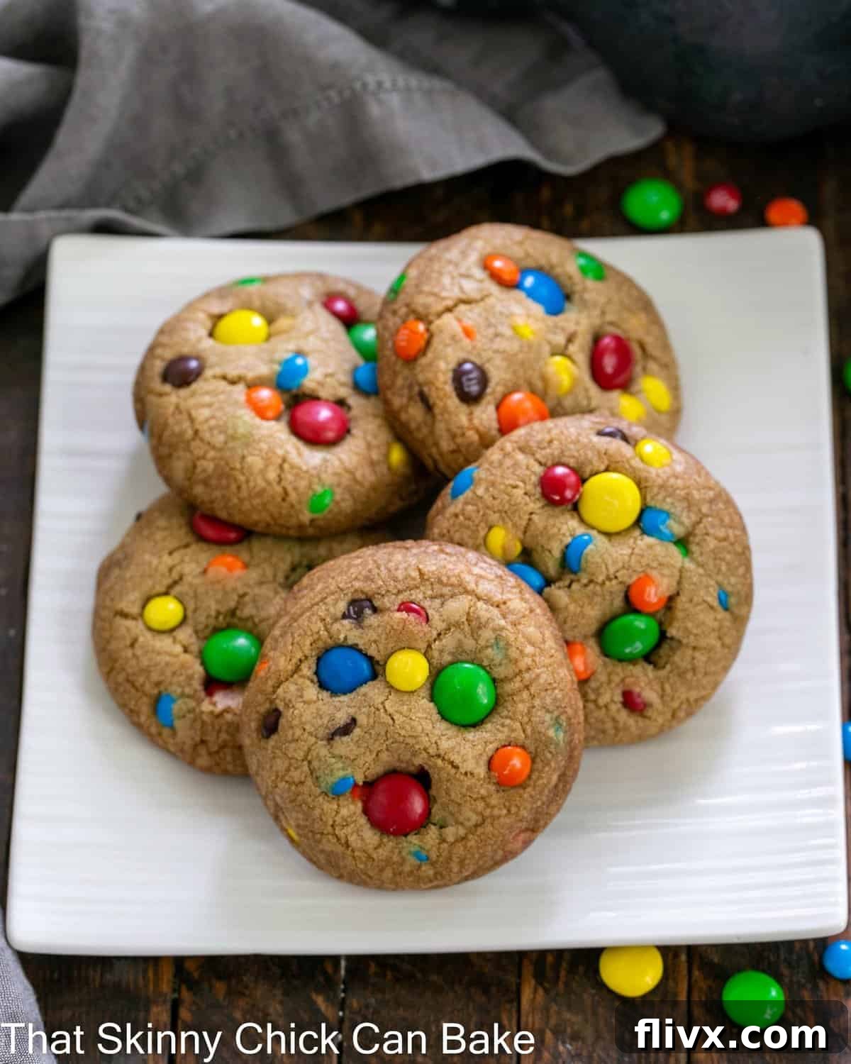 Overhead shot of five perfectly baked M&M cookies arranged on a square white plate, highlighting their vibrant colors and golden edges.