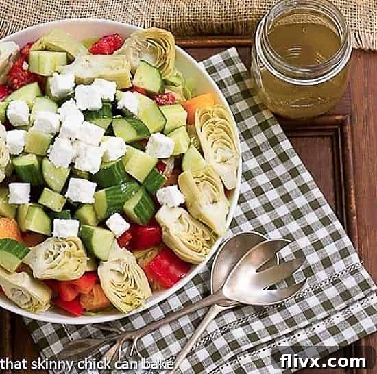Greek Salad with Feta in a serving bowl with salad serving utensils and a jar of vinaigrette.