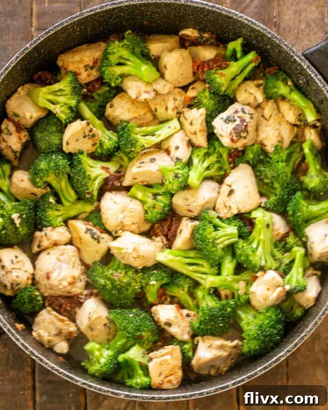 Chicken in skillet with fresh green broccoli florets, simmering gently in a sauce enriched with white wine and chicken broth.
