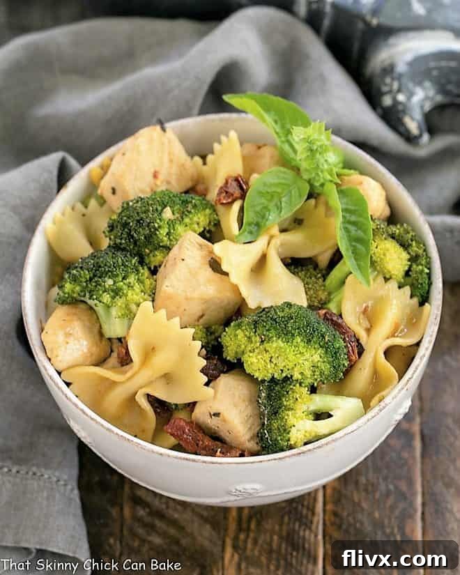 Overhead view of a white ceramic bowl filled with the finished Chicken with Broccoli, Sun-dried Tomatoes and Bow Tie Pasta, garnished and ready to be enjoyed.