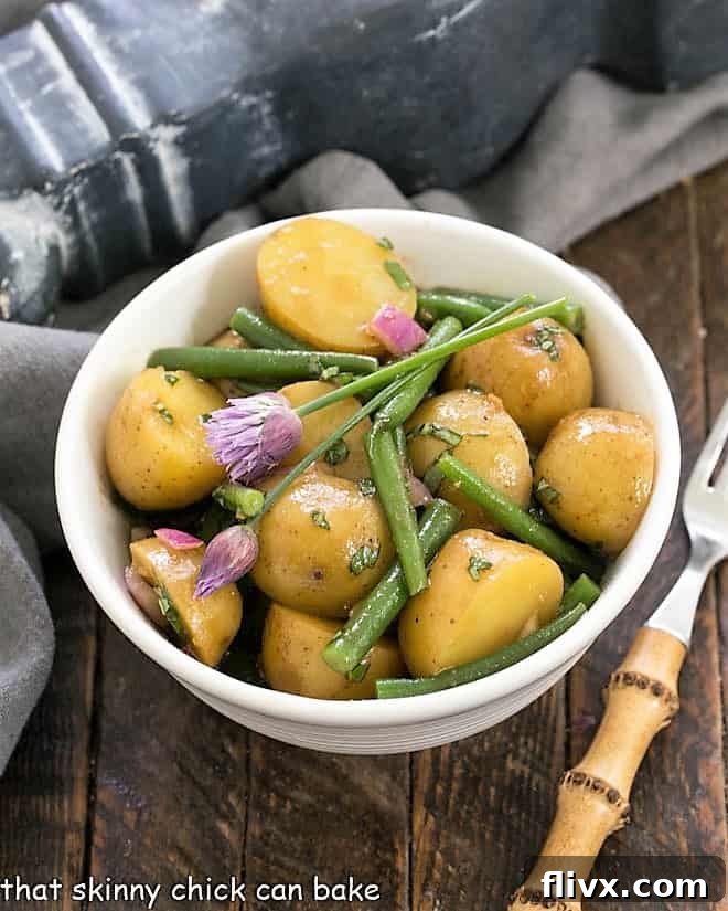 Potato and Green Bean Salad with Dijon Vinaigrette in a white bowl with a bamboo fork, showcasing its fresh ingredients.