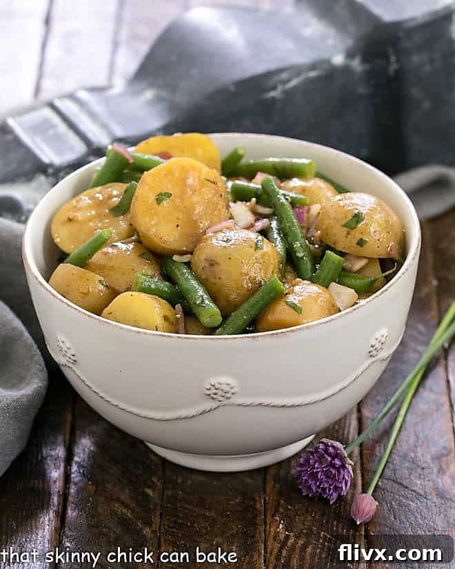 Homemade potato salad with green beans and Dijon vinaigrette in a white serving bowl, ready to be enjoyed.