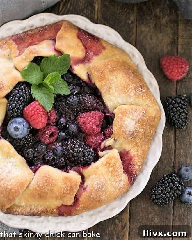 Mixed Berry Galette - a summer Fruit Tart made with sweet, seasonal berries Overhead view of a rustic berry tart on a white plate surrounded by fresh berries.