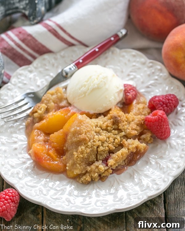 A warm Peach Raspberry Crisp on a white plate, beautifully topped with a melting scoop of vanilla ice cream, ready to be enjoyed.
