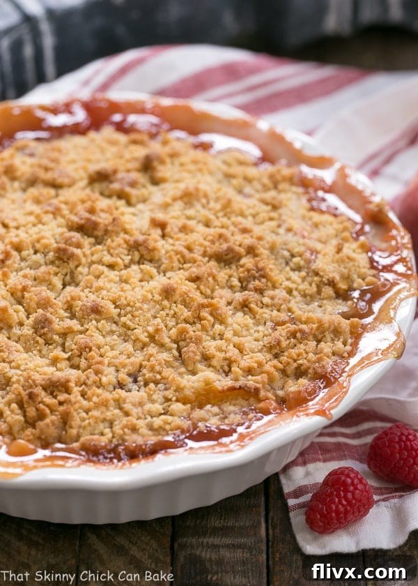 A perfectly baked Peach Raspberry Crisp, still warm in its white porcelain pie plate, showing its golden-brown topping and bubbling fruit filling.