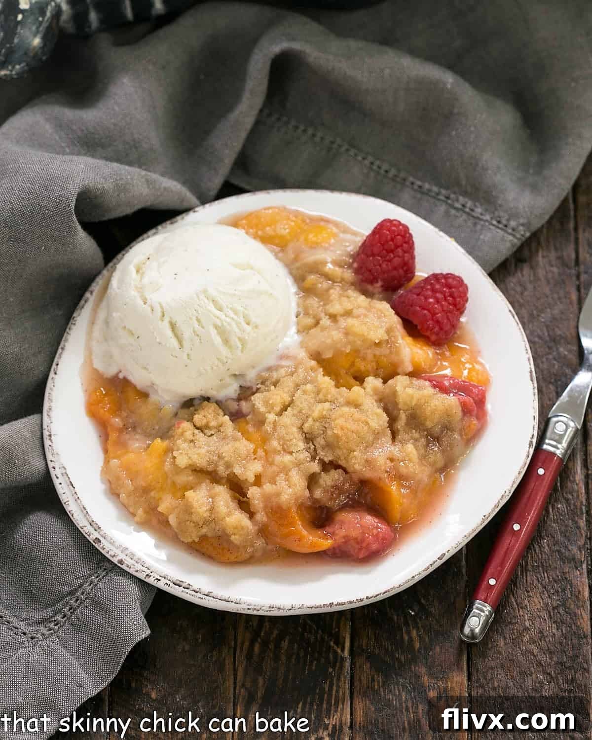 An overhead view of a freshly baked Peach Raspberry Crisp, generously topped with a scoop of vanilla ice cream, in a rustic baking dish.