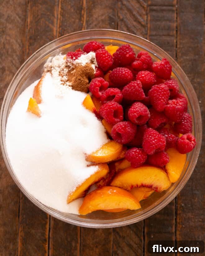 A close-up view of the peaches and raspberries in a bowl, with sugar, flour, and cinnamon added, ready for gentle mixing.