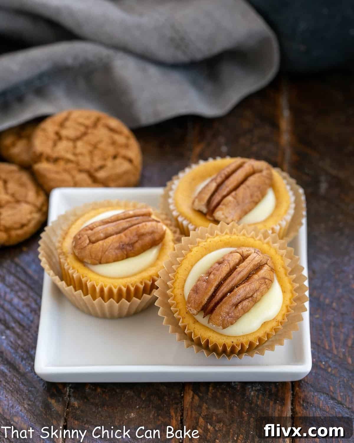 Three exquisite mini pumpkin cheesecakes artfully arranged on a square white plate, showcasing their perfect form and inviting toppings.