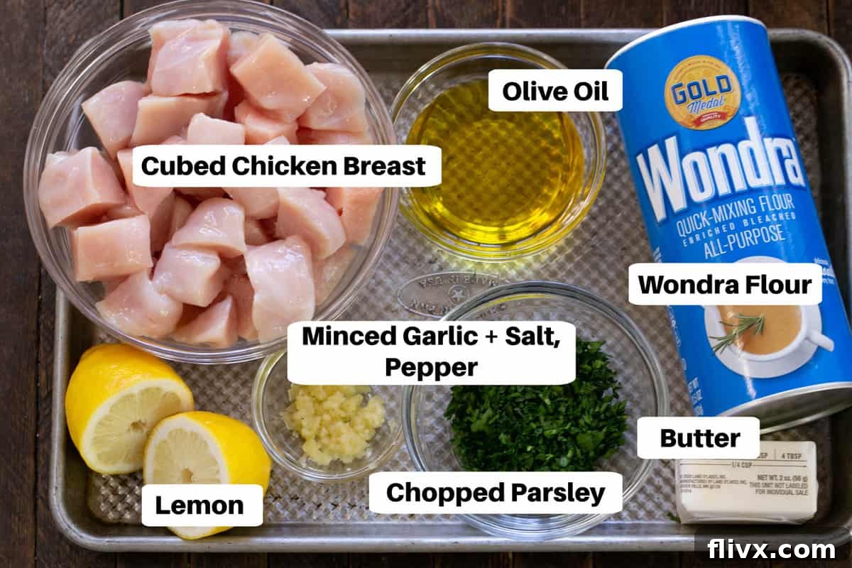 Neatly arranged ingredients for Chicken with Garlic and Parsley, including cubed chicken, garlic, parsley, lemon, and flour, all labeled on a sheet pan, ready for preparation.